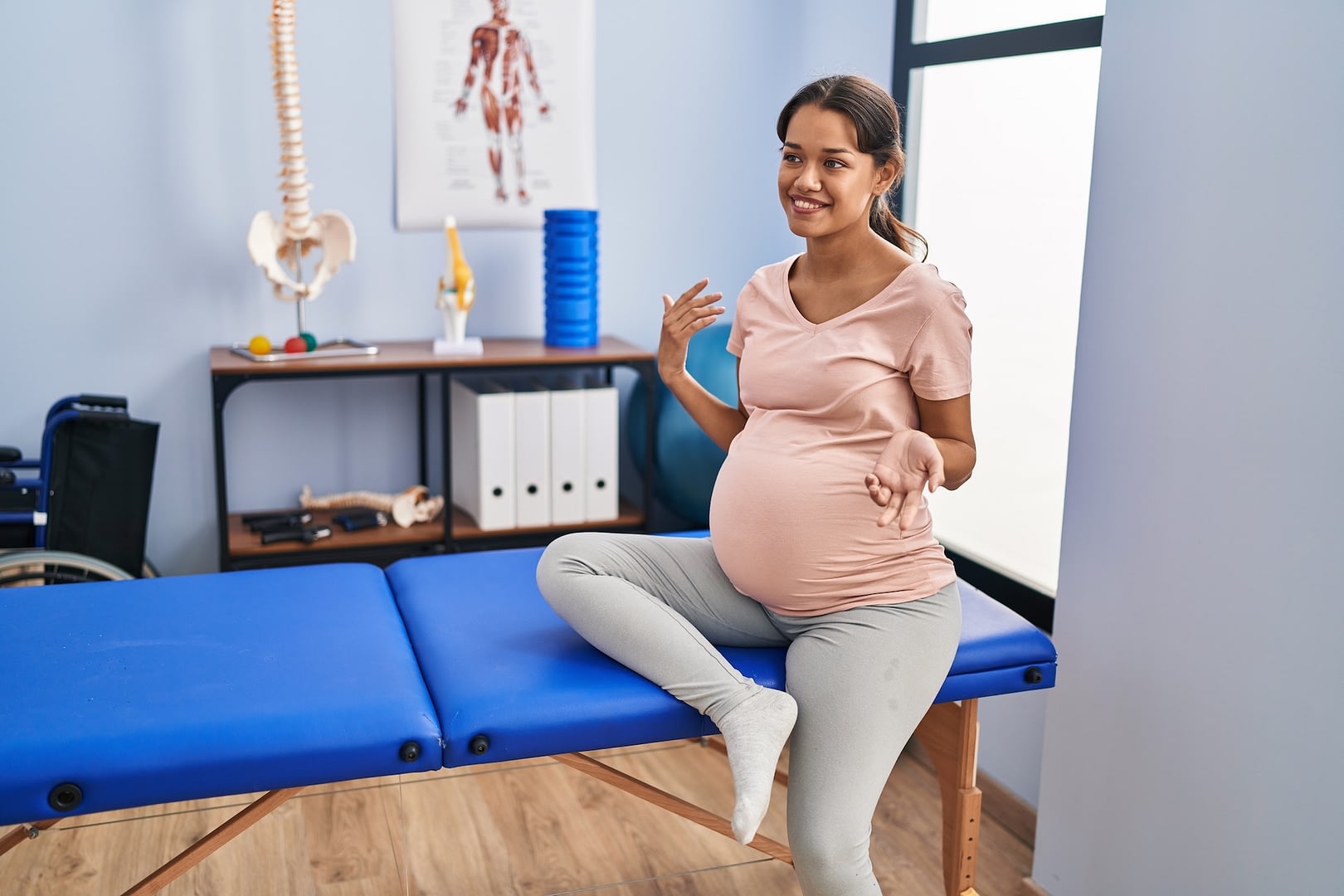 Young female pregnant patient sitting on massage table at clinic