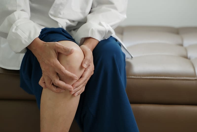 A close-up of an elderly individual holding their knee, depicting discomfort or joint pain.