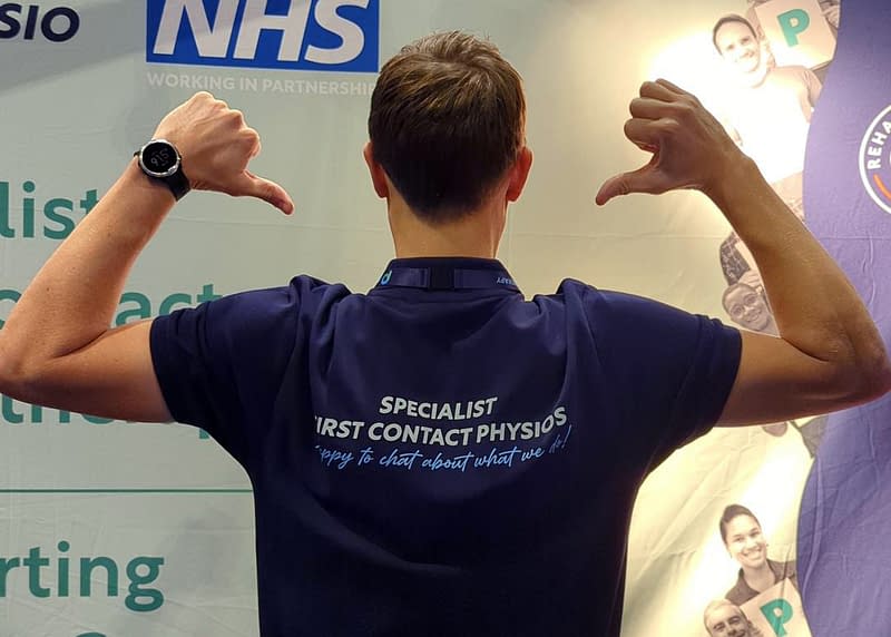 Pure Physiotherapist pointing to the words on his back, reading: Specialist first contact physios, happy to chat about what we do!